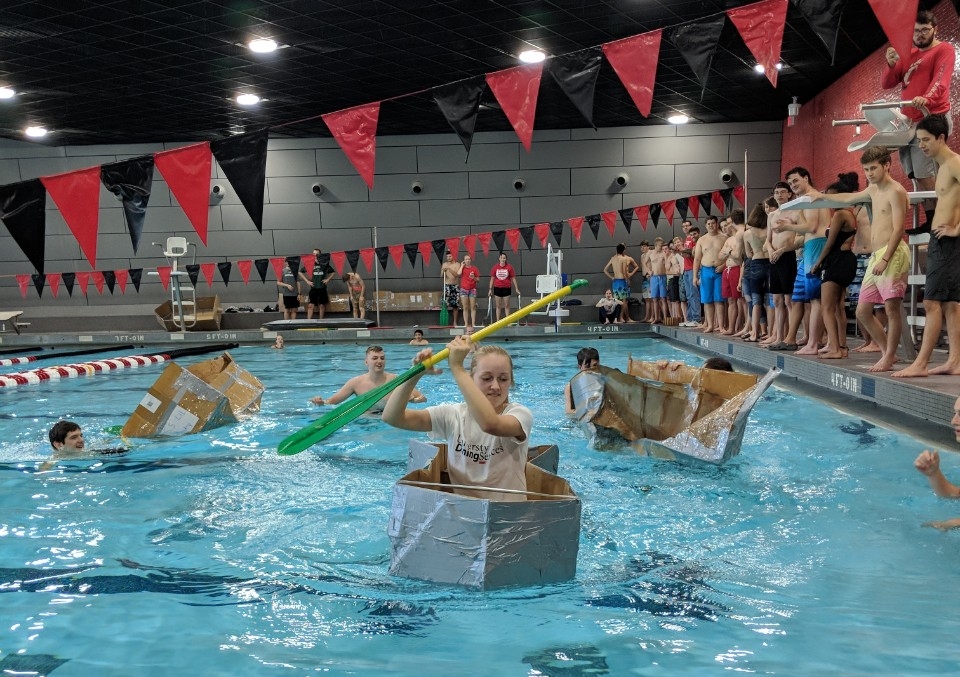 cardboard canoe race in a UC pool. One young woman is paddling her canoe while other canoes sink in the background