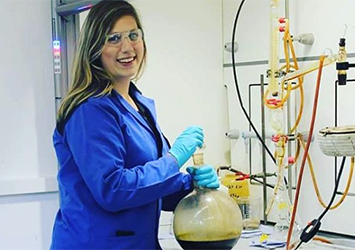Alyssa Albek, chemical engineering class of 2017, in a blue labcoat wearing blue gloves and safety glasses as she mixes a solution in a large chemical beaker.